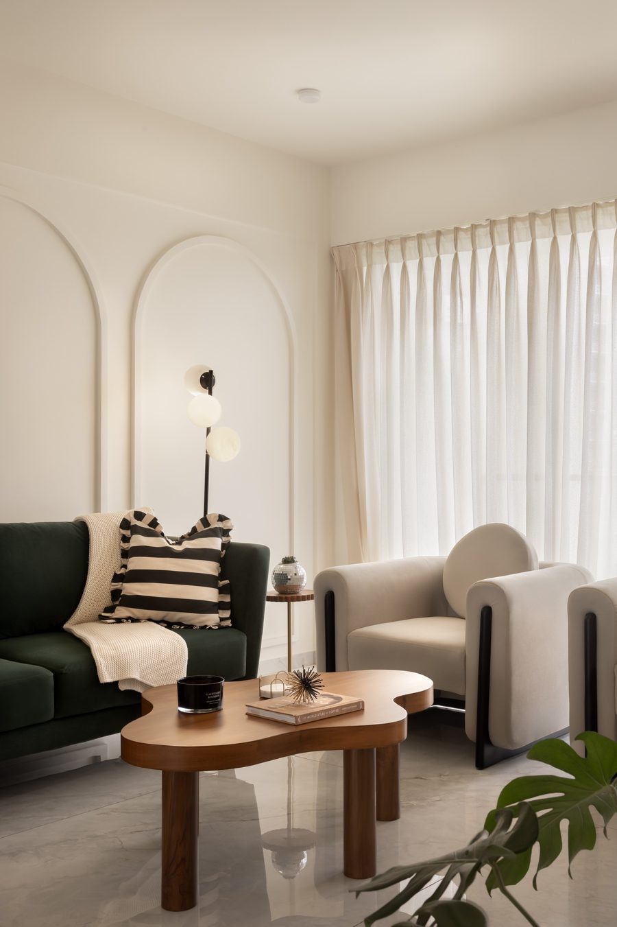 Deep-green sofa and cream armchair beneath arched wall panelling