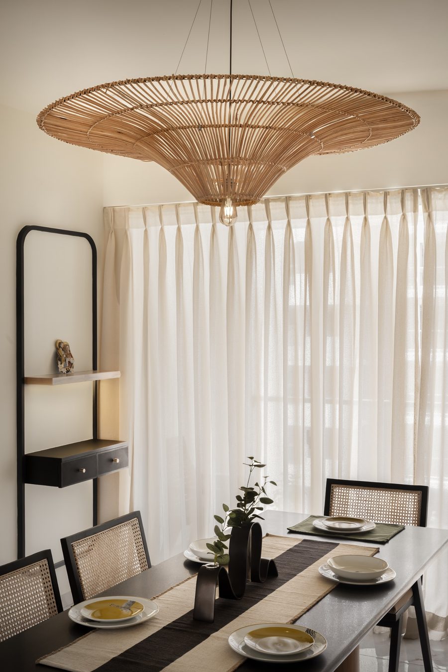 Dining table under a wide rattan pendant beside an arched mirror console