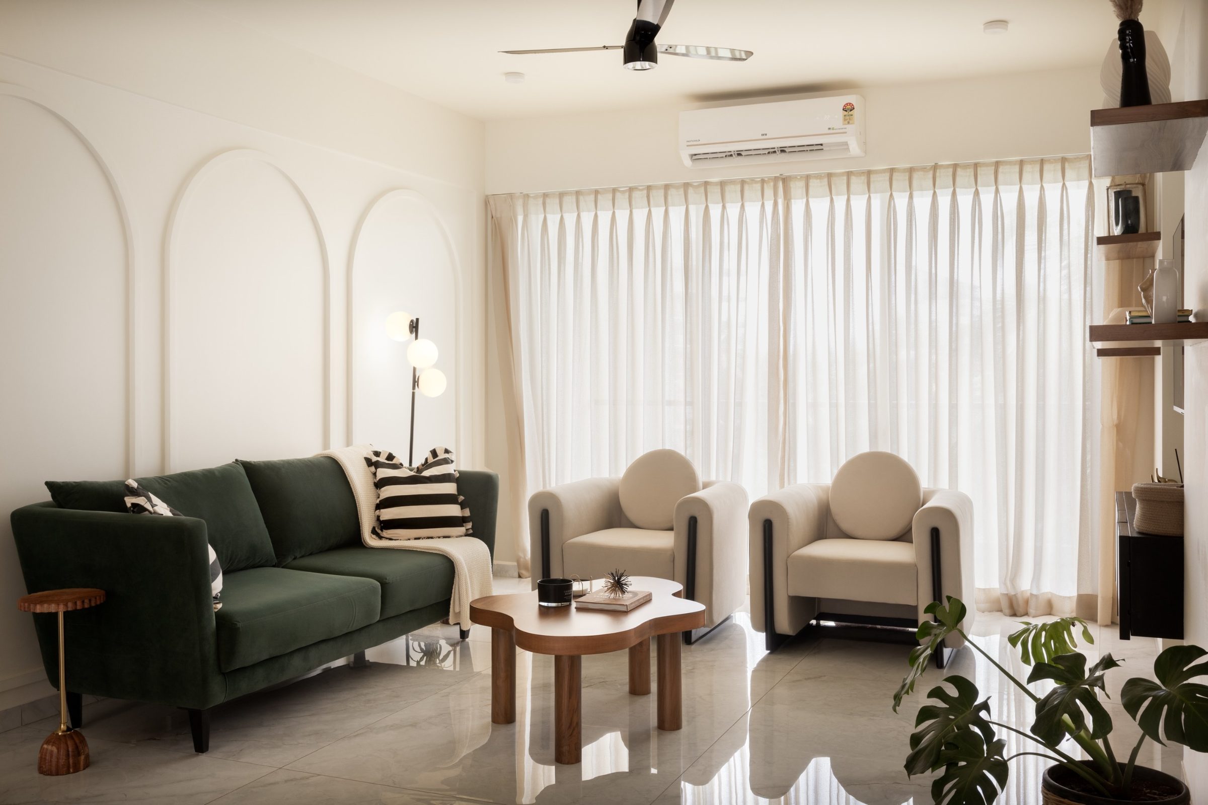 Serene living room by Svay Studio — deep-green sofa, cream armchairs and arched wall panelling in soft daylight